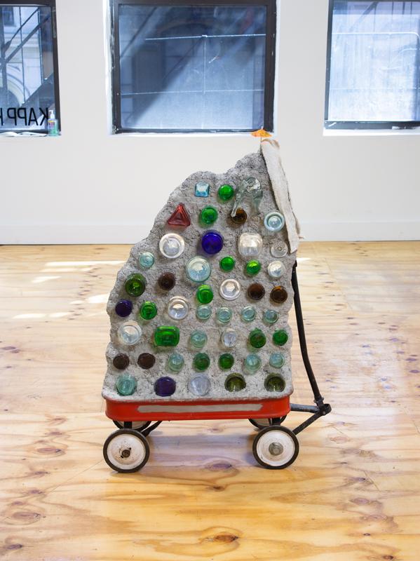 Louis Osmosis ,   Bottle Wall , 2022. Reclaimed glass bottles, concrete, wagon, threaded rod, lathe, rag, cocktail umbrella. 47 x 35 x 14 inches.