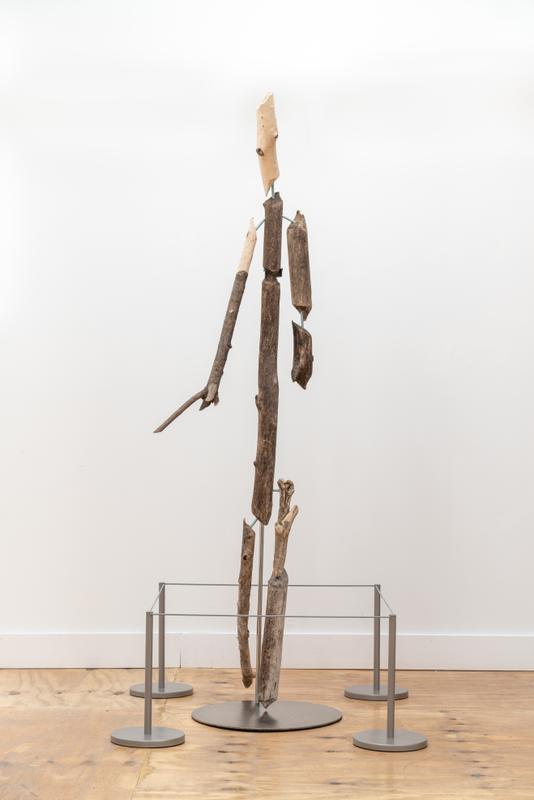 Louis Osmosis ,   Shtick Figure , 2022. Beaver-chewed wood, threaded rod, steel, epoxy, contact cement, threaded rod, rubber, stanchion. 23 x 32 x 82 inches.